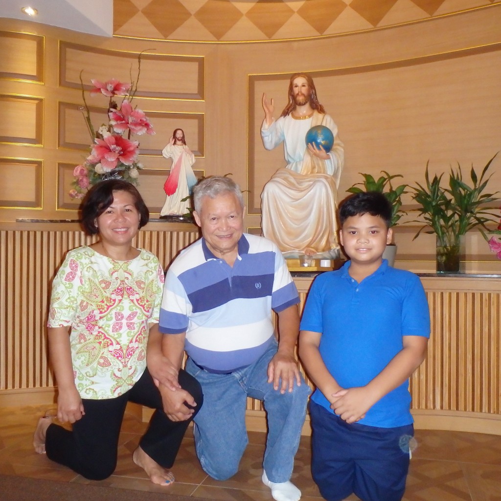The author with her husband and son inside the prayer room in Grand Lord Hotel in Bangkok, Thailand. In the background is the small statue of the Divine Mercy and Jesus holding the world on his left hand.